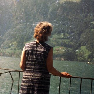 Person overlooking a lake with mountains and green slopes.