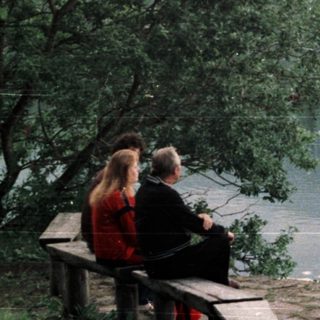 Couple sitting on bench overlooking lake and forested hillside.