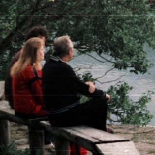 Couple sitting on bench overlooking lake and forested hillside.