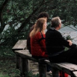 Couple sitting on bench overlooking lake and forested hillside.