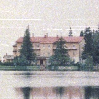 A building reflected in a still lake surrounded by trees.