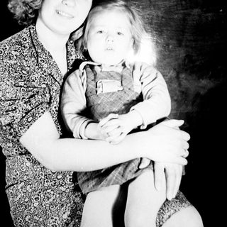 Here's a brief summary of the image: Girl holding a doll, posed in a studio setting.