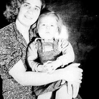 Here's a brief summary of the image: Girl holding a doll, posed in a studio setting.