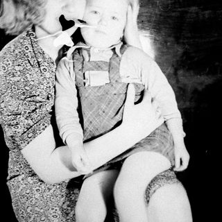 Woman holding child, both wearing masks, vintage photograph.