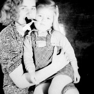 Woman holding child, both wearing masks, vintage photograph.