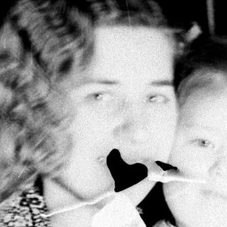Woman holding child, both wearing masks, vintage photograph.