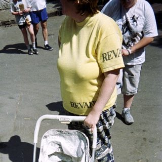 Baby in stroller with an adult in the background.