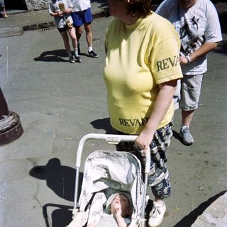 Baby in stroller with an adult in the background.