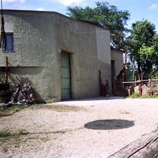 Giraffe in enclosure with building and trees in background.