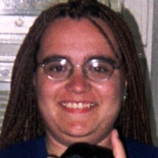 Person stands in a kitchen holding an item.