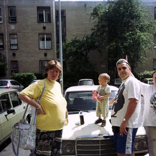 Family posing near cars in front of an apartment building.