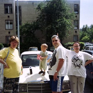Family posing near cars in front of an apartment building.