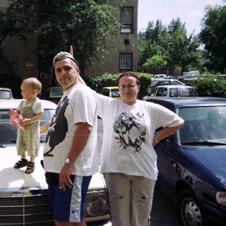Family posing near cars in front of an apartment building.