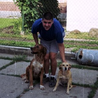 A person stands with two dogs in front of a house.