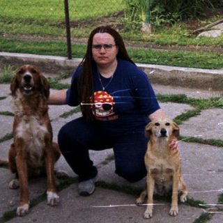 Person kneeling outdoors with two dogs in a yard.