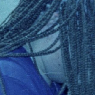 Person with braids stands near a bucket outside.