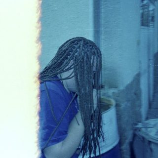 Person with braids stands near a bucket outside.