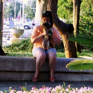 Woman sits on a ledge overlooking a harbor and flowers.