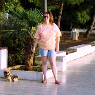 Woman and dog stand on a paved area with greenery.