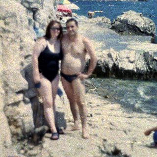 Couple standing on a rocky beach with people sunbathing.