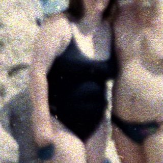 Couple standing on a rocky beach with people sunbathing.