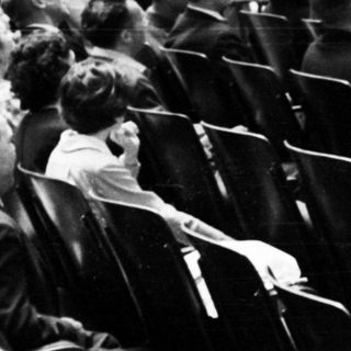 Group of men on stage, audience seated in tiered theater.