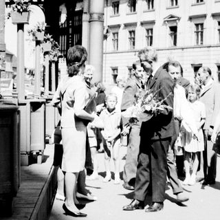 People gather around a man on a street, possibly receiving flowers.
