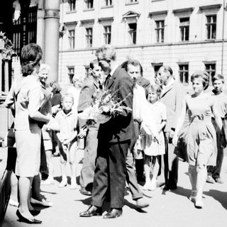 People gather around a man on a street, possibly receiving flowers.