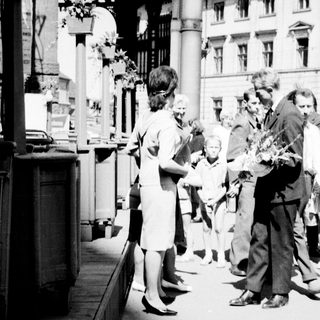 People gather around a man on a street, possibly receiving flowers.