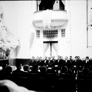 Group of men in formal wear in a grand hall.