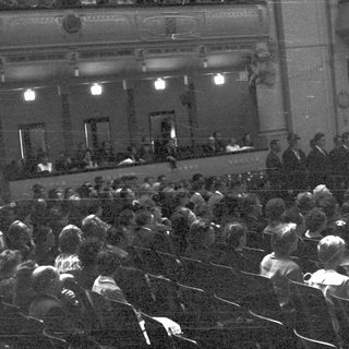 Black and white image shows a crowded theater audience.