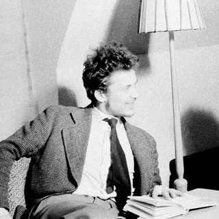 Two people converse near books and a lamp.