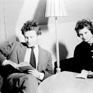 Two people reading books while seated on a couch.
