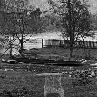 Boat rests near a river with trees and hillside.