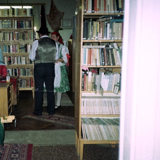 People in traditional dress stand near bookshelves in a room.