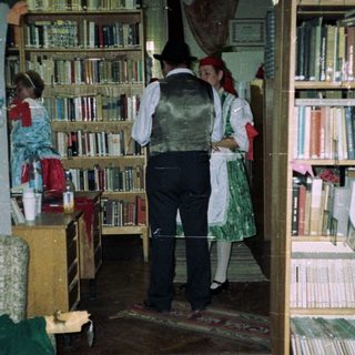 People in traditional dress stand near bookshelves in a room.