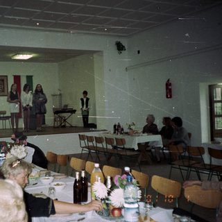 People gather in a hall with a small stage.