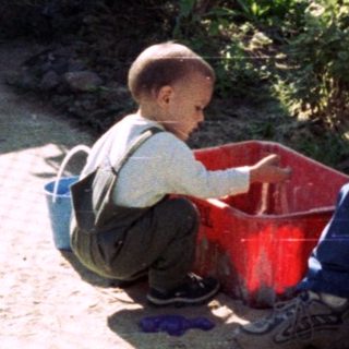 Man and child sitting outdoors, near a wall and greenery.