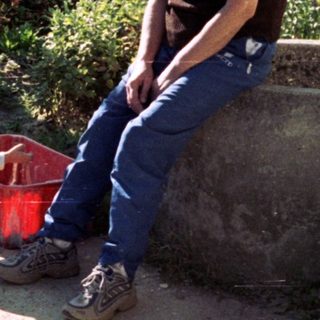 Man and child sitting outdoors, near a wall and greenery.
