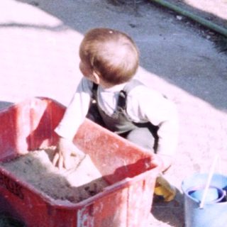 Boy plays with sand near a concrete structure and plants.