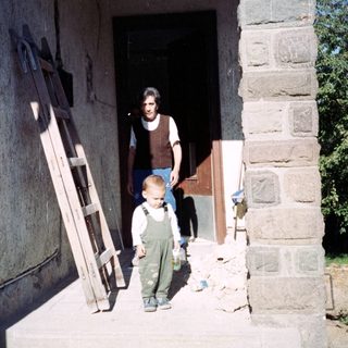 Boy stands on porch; man is inside doorway.
