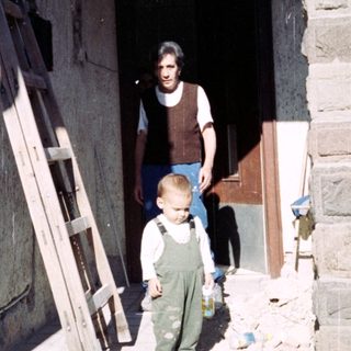 Boy stands on porch; man is inside doorway.