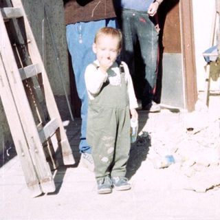 A child stands near a doorway with two men.