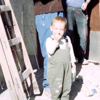 A child stands near a doorway with two men.