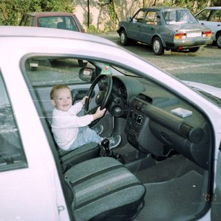 Child playfully sits in a car's driver's seat.