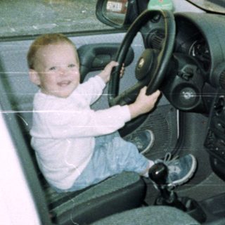 Child playfully sits in a car's driver's seat.