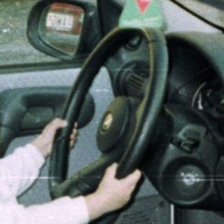 Child playfully sits in a car's driver's seat.