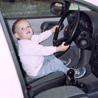 Young boy sits in a car, pretending to drive.