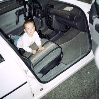 Boy crawls inside a white car, appearing playful.
