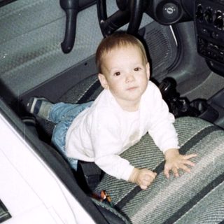 Boy crawls inside a white car, appearing playful.